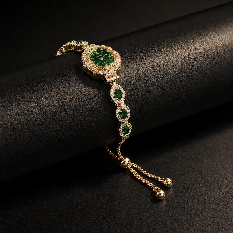 May include: A gold-tone quartz watch with a round green face, surrounded by a halo of clear crystals. The bracelet features alternating oval green stones and clear crystal accents, finished with a sliding adjustable chain and two gold-tone beads.