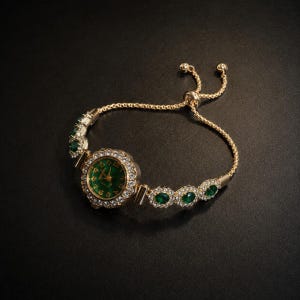 May include: A gold-tone bracelet watch featuring a round face with a deep green dial, gold numerals, and hands. The bezel and bracelet links are encrusted with clear crystals and oval-cut green stones. It has an adjustable sliding clasp closure.