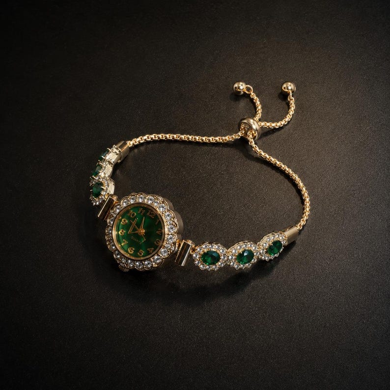 May include: A gold-tone bracelet watch featuring a round face with a deep green dial, gold numerals, and hands. The bezel and bracelet links are encrusted with clear crystals and oval-cut green stones. It has an adjustable sliding clasp closure.
