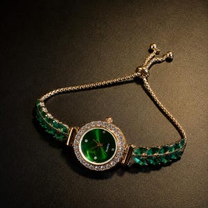 May include: A gold-tone quartz watch featuring a round green dial with small crystal markers. The bezel is encrusted with clear crystals, and the bracelet consists of gold-tone chain links accented with marquise-cut green stones on each side.