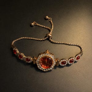 Puede incluir: Un reloj analógico dorado con esfera redonda roja y bisel incrustado con cristales transparentes. La pulsera presenta piedras circulares rojas alternadas con cristales y un cierre de cadena deslizante ajustable para el ajuste.