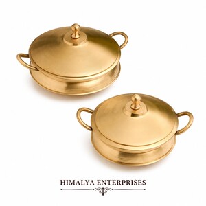 Op de afbeelding: Twee goudkleurige serveerschalen met deksel. Elke schaal heeft een afgeronde basis, een deksel met een kleine knop en twee gebogen handvatten. De tekst "HIMALYA ENTERPRISES" staat onderaan de afbeelding.