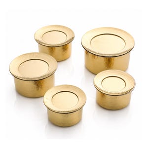 May include: A set of five round, gold-coloured metal containers with lids. Each container features a textured, hammered finish on the sides and a smooth, flat circular top. The containers vary in size, arranged in a cluster with one larger piece.
