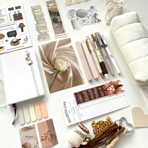 Op de afbeelding: Een collectie schrijfwaren waaronder een wit notitieboek met een koffiebedel, een leeslijst, diverse pennen, stickers met boeken, een roos en een vlinder, een wit pluche etui en een sleutelhanger met koffiethema.