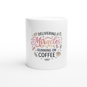 May include: A white ceramic mug featuring the text "DELIVERING Miracles RUNNING ON COFFEE" in black and gradient pink-to-orange lettering. The design includes small illustrations of baby feet, a stork, a crescent moon, and a coffee cup.