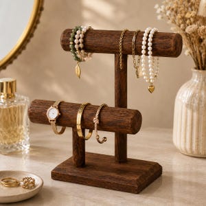 May include: A two-tiered dark brown wooden jewellery display stand featuring a horizontal bar for hanging bracelets and necklaces, and a lower bar for watches and bangles, with a rectangular base for stability and a smooth, polished finish.
