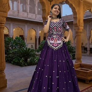 May include: A deep purple floor-length dress featuring a bodice with a white grid pattern, pink floral embroidery, and a central patch with a bird motif. The skirt is adorned with small white circular accents and has a full, pleated silhouette.