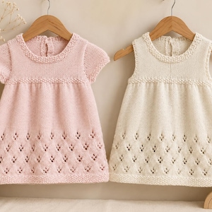 Può includere: Due abiti in maglia appesi a grucce di legno, uno rosa tenue e uno color crema. Entrambi gli abiti presentano uno scollo rotondo, maniche corte, un corpetto in maglia testurizzata e un motivo traforato a rombi sull'orlo inferiore.
