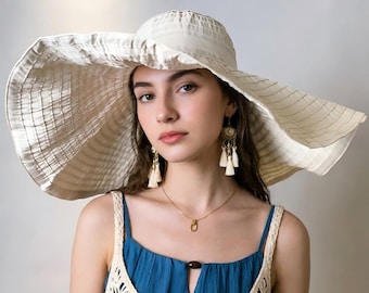 Puede incluir: Un sombrero de sol color crema de ala ancha con un diseño de tela plisada y texturizada. El sombrero presenta una copa redondeada y un ala grande y flexible. Se combina con una blusa azul sin mangas y una prenda superpuesta de ganchillo color crema.