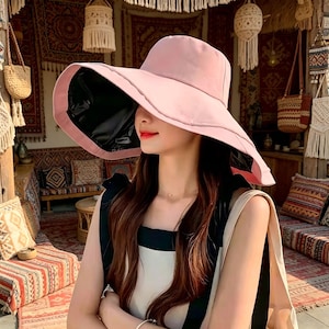 Puede incluir: Un sombrero para el sol rosa claro con ala ancha y parte inferior negra. El sombrero est&aacute; dise&ntilde;ado para dar sombra y tiene una forma estructurada. Un accesorio de moda para d&iacute;as soleados y actividades al aire libre.