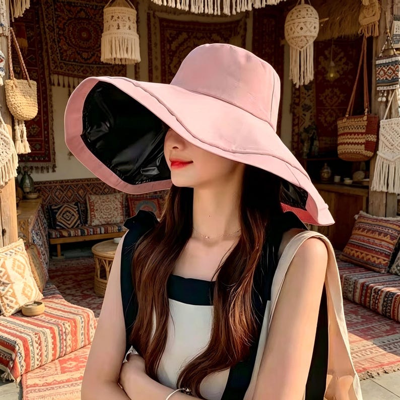Puede incluir: Un sombrero para el sol rosa claro con ala ancha y parte inferior negra. El sombrero est&aacute; dise&ntilde;ado para dar sombra y tiene una forma estructurada. Un accesorio de moda para d&iacute;as soleados y actividades al aire libre.