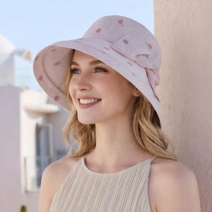 Puede incluir: Un sombrero para el sol rosa claro con ala ancha y lazo. El sombrero está decorado con pequeños lunares rosas oscuros. Hecho de tela suave, está diseñado para proteger del sol. Un accesorio de moda.