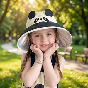 May include: A wide-brimmed sun hat featuring a cream-coloured crown and a black brim. The hat is designed with a panda face graphic on the front, complete with two black rounded ears protruding from the top of the crown and black eye patches.