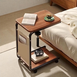 May include: A mobile side table with a dark wood top and a lower shelf. The table has a black metal frame and a beige magazine holder. An open book, a cup of coffee, and a retro clock are on the table.