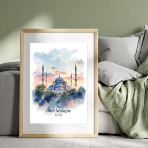 Puede incluir: Impresión en acuarela enmarcada de la Mezquita Azul en Turquía. La obra representa la mezquita con sus cúpulas y minaretes, sobre un cielo de atardecer. El texto en la parte inferior dice "The Blue Mosque Turkey". El marco es de madera clara.