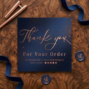May include: A square navy blue card with rose gold foil text that reads Thank you For Your Order WE WOULD LOVE TO HEAR YOUR FEEDBACK leave a review! followed by five stars. The card is surrounded by copper pens, navy blue ribbon, and wax seals.