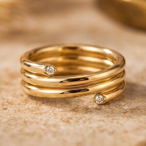 Puede incluir: Un anillo de oro tipo bypass con un diseño de múltiples espirales que se envuelve alrededor del dedo. El anillo está hecho de oro amarillo pulido y está acentuado con dos pequeños diamantes blancos redondos y claros en los extremos abiertos.