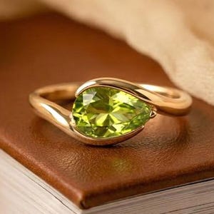 Może przedstawiać: Biały ceramiczny kubek z czarnym uchwytem i napisem "But First, Coffee" czarną, pogrubioną czcionką. Kubek stoi na białej powierzchni.