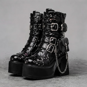 May include: A pair of black patent platform boots featuring a high block heel, lace-up front, and multiple adjustable straps with silver buckles. The boots are decorated with small silver star studs and include a detachable mini pouch on a chain.