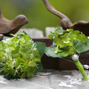 May include: Two green floral arrangements with white accents. One arrangement has a pearl embellishment and is tied with a green ribbon.