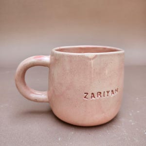 May include: A white ceramic mug with a black handle and the text "But First, Coffee" in a black, bold font. The mug is on a white surface.