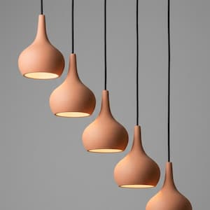 Pode incluir: Cinco luminárias suspensas cor de terracota em forma de gota penduradas em cabos pretos contra um fundo cinza. As luzes são iluminadas por dentro, emitindo um brilho quente.