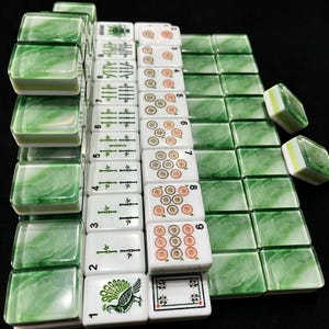 May include: A set of rectangular mahjong tiles featuring a white base with green marbled backs. The tiles display various traditional symbols, including bamboo stalks, circular patterns, a peacock illustration, and floral motifs in green and orange.