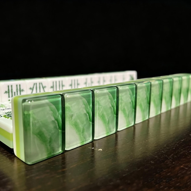 May include: A row of rectangular mahjong tiles featuring a translucent green and white marbled design on the front faces. The tiles have a layered construction with a clear green top section, a light green middle layer, and a white base.
