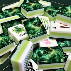 Peut inclure: Un ensemble de tuiles de mah-jong pr&eacute;sentant un motif marbr&eacute; vert fonc&eacute; et dor&eacute; sur la face sup&eacute;rieure, avec des c&ocirc;t&eacute;s superpos&eacute;s blancs et vert clair. Certaines tuiles affichent des symboles de dragon, de bambou et de fleurs.