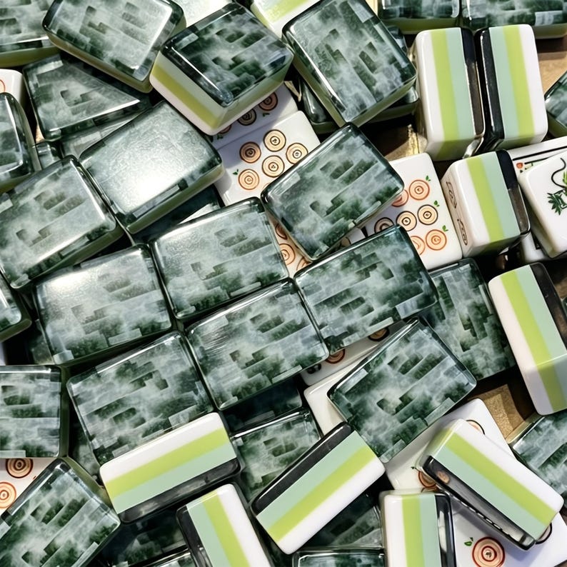 May include: A collection of rectangular mahjong tiles featuring a mix of dark green marbled patterns and white tiles with light green stripes. Some tiles display orange circular symbols, while others show green line art designs on their white surfaces.