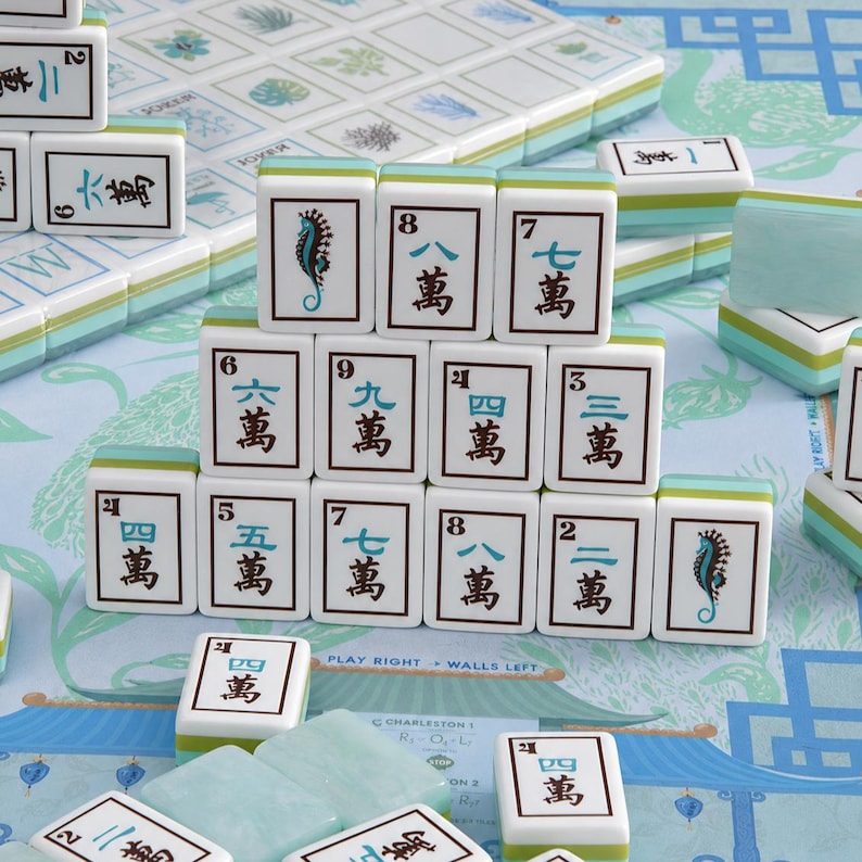 May include: A set of white mahjong tiles with light blue and green accents, featuring black Chinese characters and seahorse illustrations. The tiles are arranged in a pyramid formation on a light blue game board with printed text and patterns.