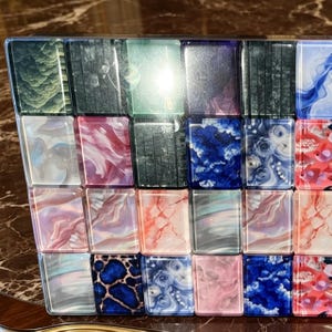 May include: A rectangular set of mahjong tiles arranged in a grid, featuring a variety of colourful designs including floral patterns, marbled textures, blue and pink swirls, dark green foliage, and animal print motifs on a glossy, smooth surface.