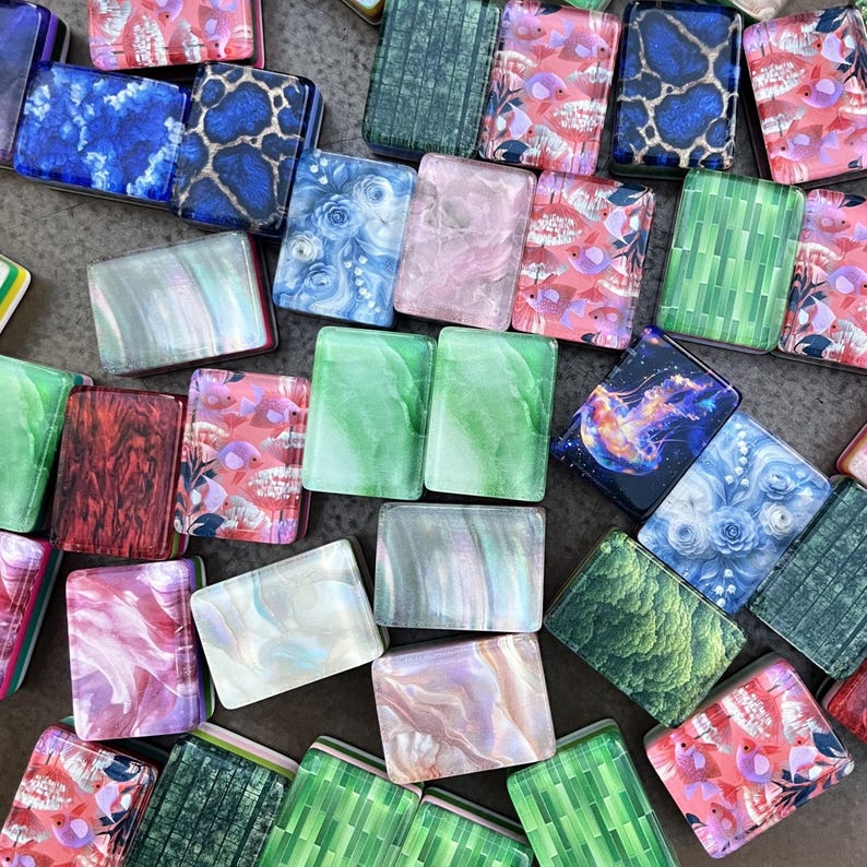 May include: A collection of rectangular tiles featuring diverse patterns including blue and green marble, floral motifs, pink fish illustrations, a glowing jellyfish, and geometric green grids, all with a smooth, glossy, and reflective surface finish.