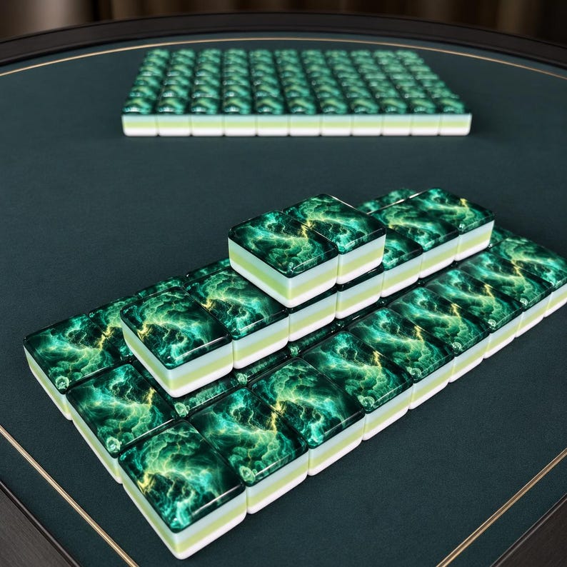 Peut inclure: Un ensemble de tuiles de mah-jong rectangulaires pr&eacute;sentant un motif de marbre vert &eacute;meraude et dor&eacute; tourbillonnant sur la face sup&eacute;rieure. Chaque tuile poss&egrave;de une base blanche &eacute;paisse et est dispos&eacute;e sur une surface vert fonc&eacute; bord&eacute;e d'or.