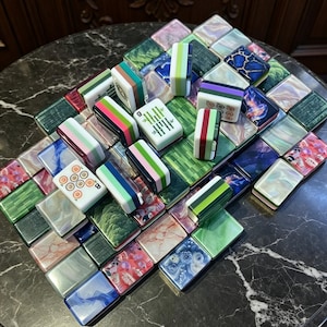 May include: A collection of rectangular mahjong tiles featuring a variety of patterns, including solid colours, marbled textures, floral prints, and traditional bamboo and circle markings, arranged in a scattered, overlapping formation.