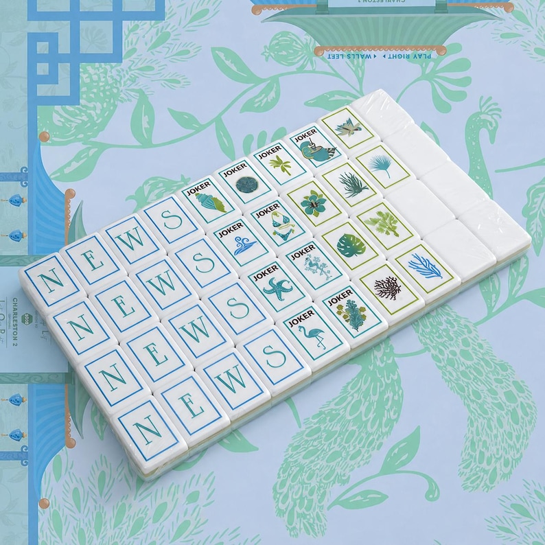May include: A set of rectangular white mahjong tiles arranged in a grid. The tiles feature blue lettered tiles spelling NEWS, tiles labeled JOKER with various tropical illustrations like flamingos, starfish, and palm trees, and blank white tiles.
