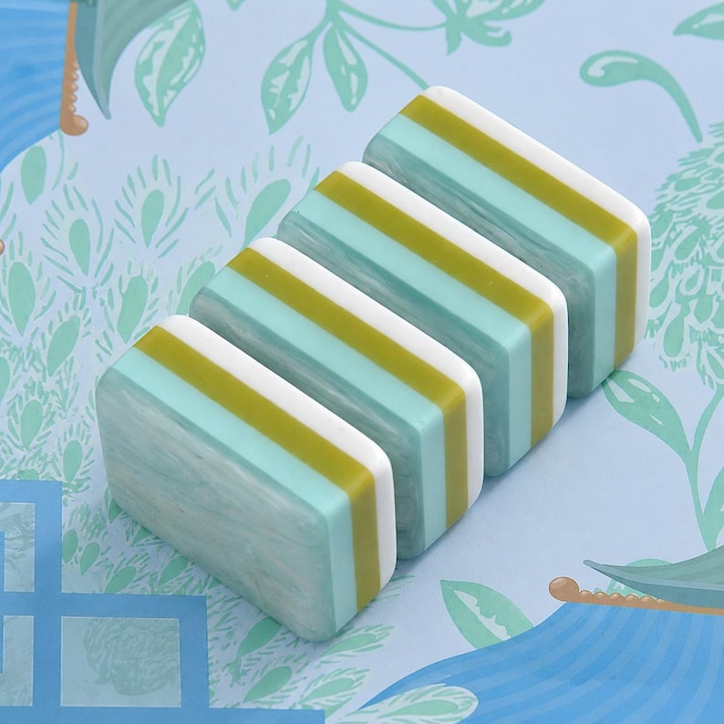 May include: Four rectangular tiles arranged in a row, each featuring a layered design with a marbled light blue section, a solid olive green stripe, and a solid white stripe. The tiles have a smooth, glossy finish and uniform dimensions.