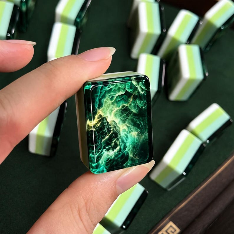 Peut inclure: Une tuile de mah-jong rectangulaire pr&eacute;sentant une surface vert fonc&eacute; brillante avec un motif tourbillonnant rappelant une n&eacute;buleuse, rehauss&eacute; de touches vert vif et jaune. Les c&ocirc;t&eacute;s sont blancs avec une bande vert p&acirc;le, comme les autres tuiles.