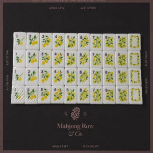 May include: A set of white rectangular mahjong tiles arranged in a grid, featuring yellow lemon illustrations and black numbers one through nine, with a zero tile decorated with a lemon wreath. The tiles are partially wrapped in clear plastic film.