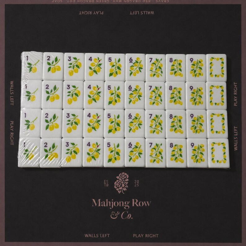 May include: A set of white rectangular mahjong tiles arranged in a grid, featuring yellow lemon illustrations and black numbers one through nine, with a zero tile decorated with a lemon wreath. The tiles are partially wrapped in clear plastic film.