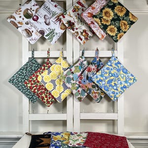 May include: A set of three ceramic mugs with a speckled, cream-colored glaze. Each mug features a different hand-painted floral design in shades of blue, green, and yellow. The mugs have a simple, modern shape.