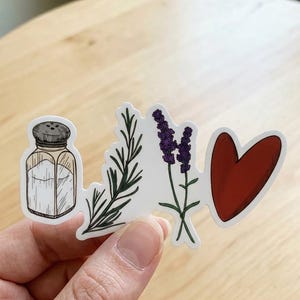May include: A die-cut sticker featuring a sequence of four illustrations: a glass salt shaker with a grey lid, a green sprig of rosemary, two purple lavender stems, and a solid red heart shape, all outlined in white on a clear backing.