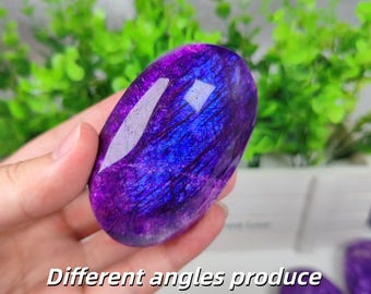 Puede incluir: Una piedra preciosa de labradorita ovalada y pulida que muestra una vibrante iridiscencia púrpura y azul eléctrico en su superficie. La piedra presenta una textura suave y reflectante con fracturas internas. El texto en la imagen dice: Different angles produce different light effects.
