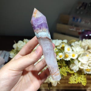 May include: A polished crystal point featuring a pointed tip, displaying a gradient of deep purple amethyst at the top, transitioning into distinct horizontal bands of white, gray, and brown agate layers, ending in a translucent, pale base.