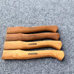 Könnte beinhalten: Vier hölzerne Axtstiele, horizontal angeordnet, jeder mit einem geschwungenen Griff und einem geraden oberen Teil. Die beiden unteren Stiele sind hellbraun mit sichtbarer Maserung und dem Text Wetterlings Genuine Hickory versehen.