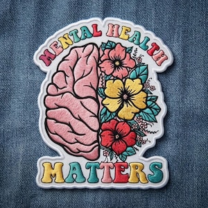 May include: An embroidered patch featuring a split design of a pink brain on the left and colorful flowers on the right. The text MENTAL HEALTH is arched across the top and MATTERS is at the bottom in multi-colored, bold, rounded lettering.