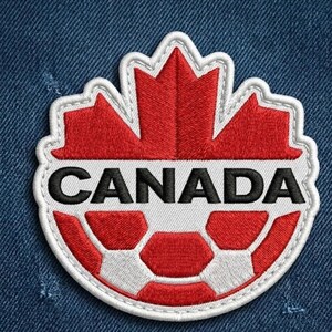 May include: A circular embroidered patch featuring a red maple leaf at the top and a white and red soccer ball pattern at the bottom. The word CANADA is stitched in bold black capital letters across a white horizontal band in the center.