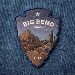 May include: An arrowhead-shaped embroidered patch featuring a desert landscape with brown mountains, a saguaro cactus, and a starry night sky. The text reads BIG BEND TEXAS and 1944 in white thread. The patch has a dark blue border and is stitched.