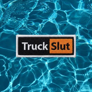 May include: A rectangular embroidered patch with a white border. The left side features the word Truck in white text on a black background, while the right side features the word Slut in black text on an orange background, creating a bold contrast.