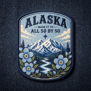 May include: A rectangular embroidered patch with rounded corners featuring a mountain landscape, a winding river, and blue flowers. The text reads ALASKA MADE IT TO ALL 50 BY 50. The design includes a compass star, clouds, and pine trees in shades of blue, white, and green.